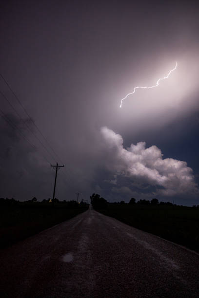 Lightning strikes behind power lines and a street on a stormy day