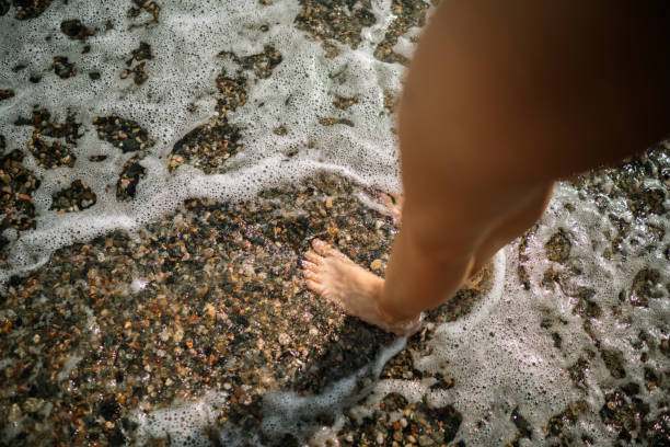 A kid standing in shallow water on a pebble beach