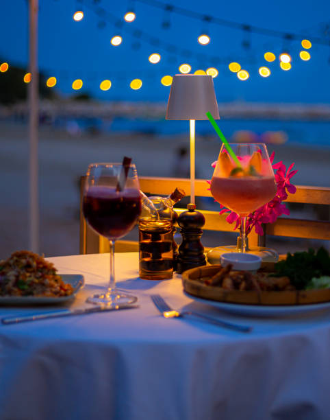 istock Beachside dinner table,Beachside dinner table with one large challah, two bottles of red wine, two wine glasses, two tea lights in jars, one small vase with flowers, at night, with hanging light nearby in background. 2156064613