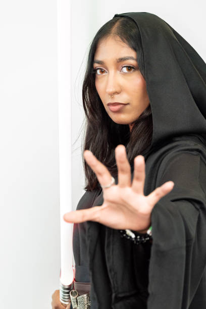 istock Woman in robes wields a light sword against a white wall backdrop 2156068356