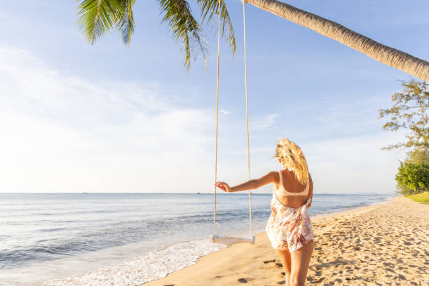 istock Woman Walking Towards a Swing on a Tropical Beach 2156072472