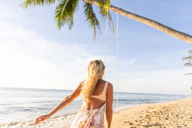 istock Woman Walking Towards a Swing on a Tropical Beach 2156072473