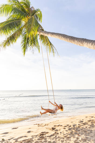 istock Woman Swinging on a Palm Tree Swing by the Beach 2156072547