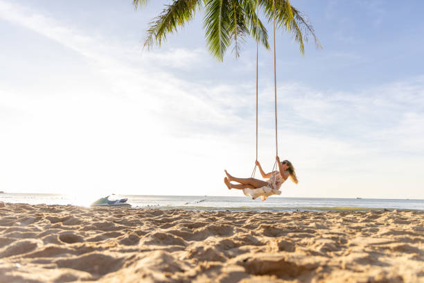 istock Woman Swinging on a Palm Tree Swing by the Beach 2156072614