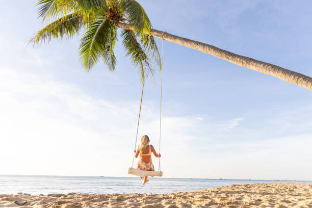 istock Woman Enjoying a Swing on a Palm Tree by the Beach 2156072700