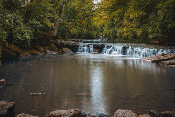 istock Serene waterfall cascades through rocks and trees, mirrored in the water 2156073302