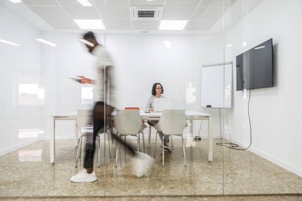 istock Blurred Man Walking Past Conference Room With Woman Working at Table 2156073983