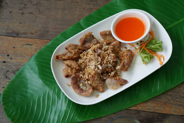 istock Deep-fried pork intestines sprinkled with fried garlic, fried kaffir lime leaves and fried dried chilies and spicy dipping sauce in a white plate placed on a banana leaf. 2156077160