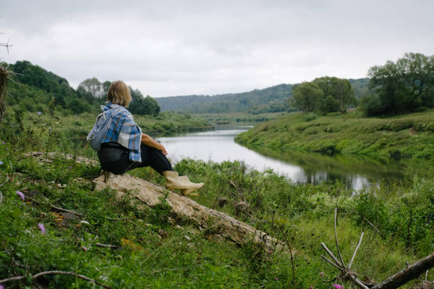istock Woman sitting on a stone on the river bank 2156077453