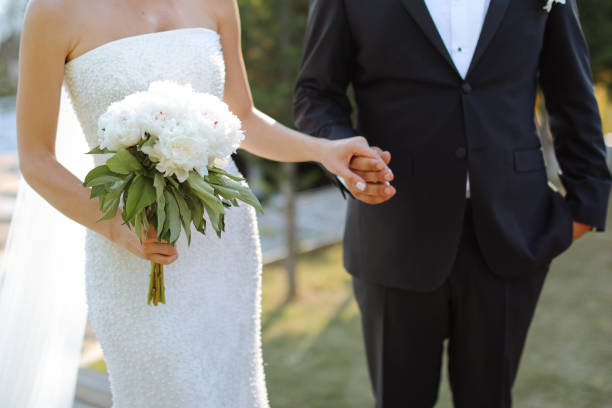 Bride and groom outdoors on a wedding day Happy bride and groom on their wedding hugging. Closeup Bride holding a bouquet hands of bride and bridegroom in wedding marriage ceremony stock pictures, royalty-free photos & images