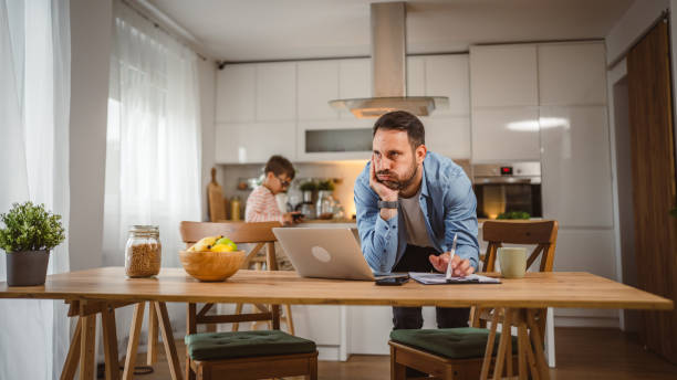 istock Exhausted man father work at home on laptop with son in the background 2156087657