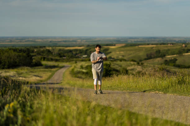 Athletic man taking a break after sports training and using smart watch on the road in nature on summer day.