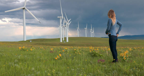 istock Young woman in meadow under wind turbines 2156104255