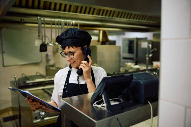 istock Happy female chef talking on the phone while going through paperwork in the kitchen. 2156105437