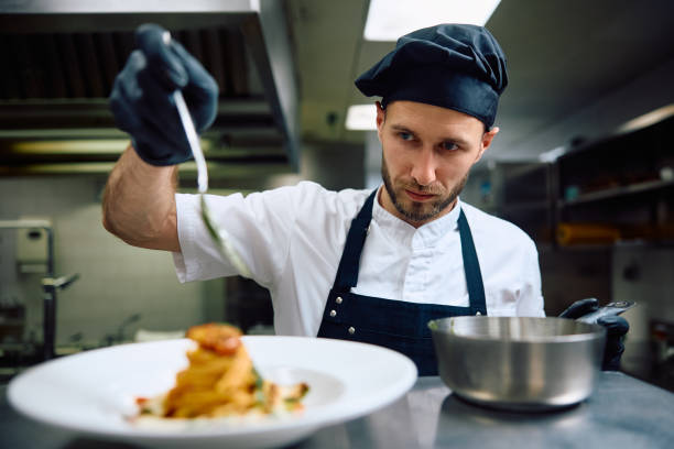 istock Professional cook pouring sauce while serving pasta on plate. 2156105628