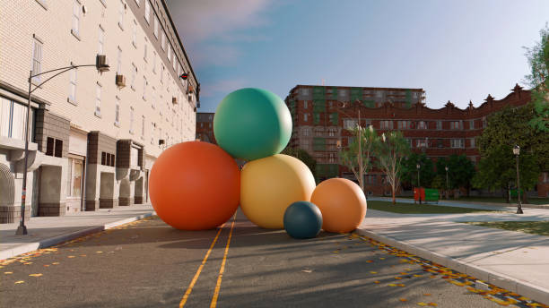 City street scene with several large, colorful balls scattered across the road. The balls vary in size and color, including orange, green, yellow, and blue. They appear to be out of place in the urban setting, which includes brick buildings, streetlights, and trees. The scene is surreal and whimsical, blending everyday city life with unexpected, oversized objects.