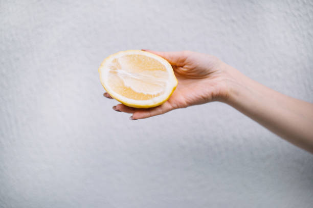 istock Woman hand holding halved lemon on white wall background 2156125700