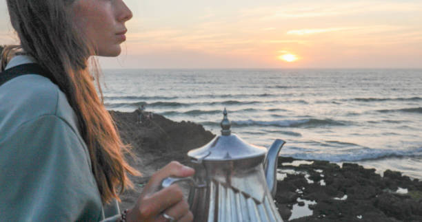 istock Young woman enjoys tea on beach at sunset 2156128394