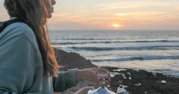 istock Young woman enjoys tea on beach at sunset 2156128416