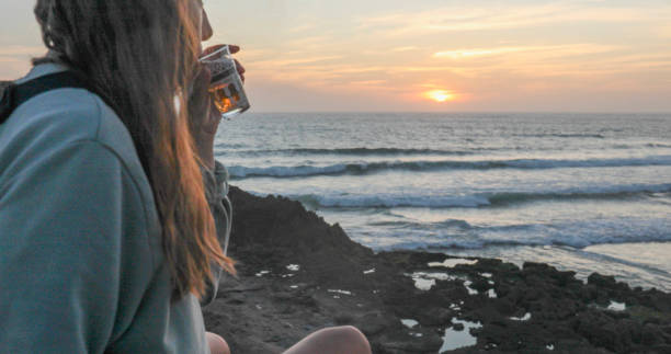 Young woman enjoys tea on beach at sunset