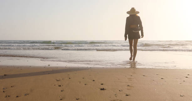 istock Young woman walks along beach at sunrise 2156128534