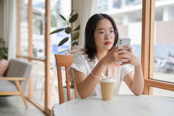 istock A young Asian woman is reading messages on her smartphone while sitting in a minimalist cafe. 2156128656