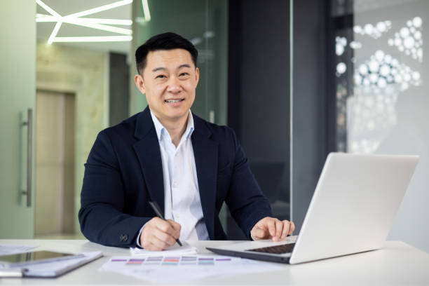 istock Asian mature man working on laptop in modern office setting 2156129928
