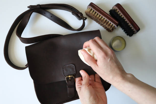 Photo process of cleaning leather products. Human hands. White background. Photo process of cleaning leather products. Crazy horse leather bag. Human hand with a sponge. Brushes and wax are nearby. The bag is brown. White background. leather care stock pictures, royalty-free photos & images
