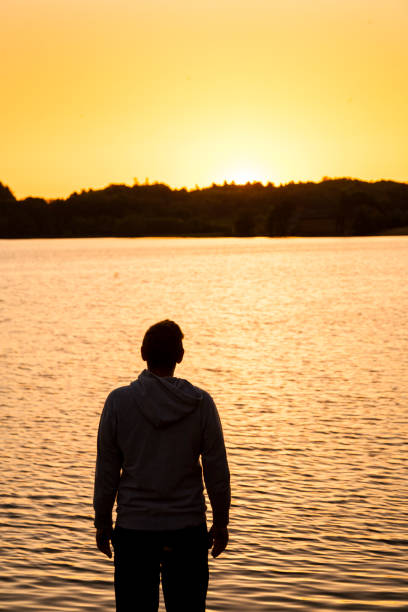 istock middle aged man standing in silhouette with back to camera looking over sea at a yellow sunrise 2156149901