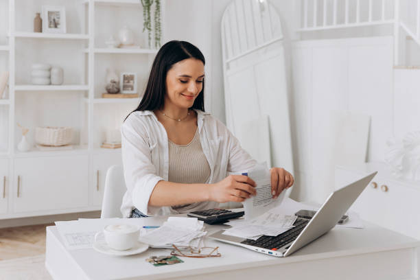 istock Young woman managing home finances, smiling while sorting receipts, calculating expenses, laptop open, coffee cup nearby, glasses and papers scattered, financial planning and organization 2156153733