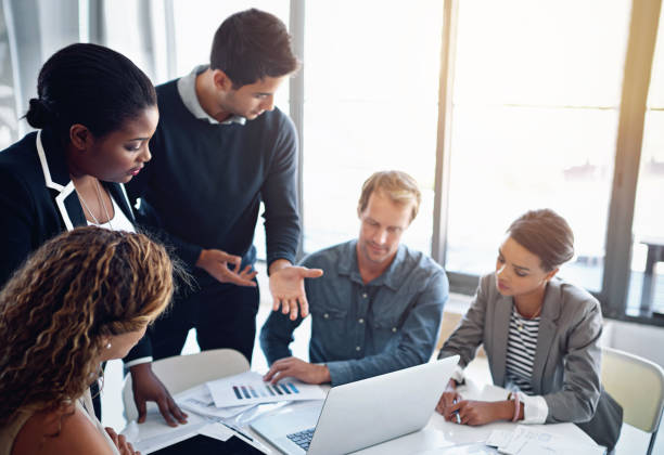 istock Business people, laptop and cooperation with conversation, group and professional in modern office. Diversity, employees and coworkers with ideas, collaboration and teamwork with document and meeting 2156157890