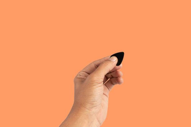 istock Black male hand holding a guitar pick isolated on orange background 2156160827