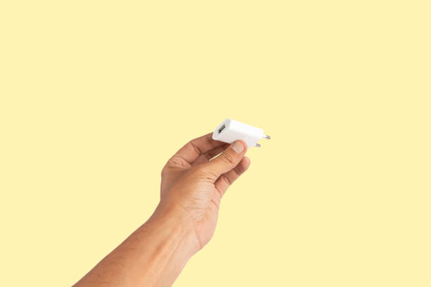 istock Black male hand holding a USB charger plug isolated on yellow background 2156161027