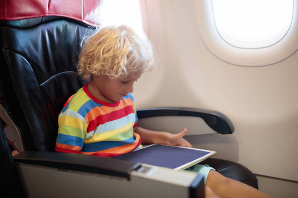 Child in airplane. Kid in air plane sitting in window seat. Flight entertainment for kids. Traveling with young children. Kids fly and travel. Family summer vacation. Little boy with toy in airplane.