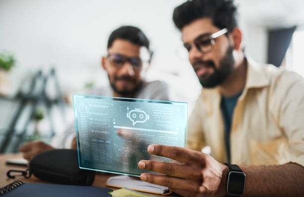 istock Two Indian men working together on a tablet with digital projection screen with hologram representing technologies of the future. Working on AI Chatbot development and accebility 2156165257