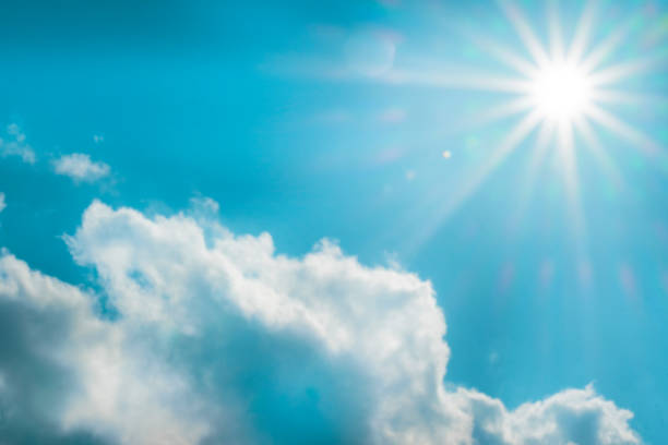 Cloud and bright sun with long rays on a bright blue sky.Sky. Heaven background.Bright sunny summer weather background.Beautiful natural background in blue and white colors
