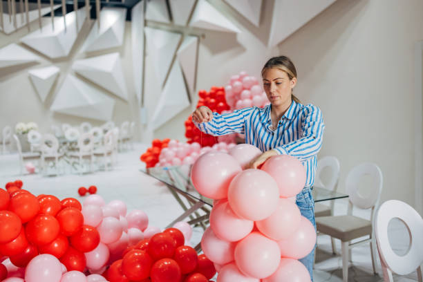 istock Female decorator arranges balloon decorations, connecting them with a thin ribbon and making a column out of them 2156168360