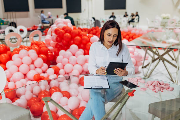 istock Female decorator is sitting at a table in a restaurant using a digital tablet. The tablet shows detailed plans and sketches for the decoration and organization of the party 2156169620