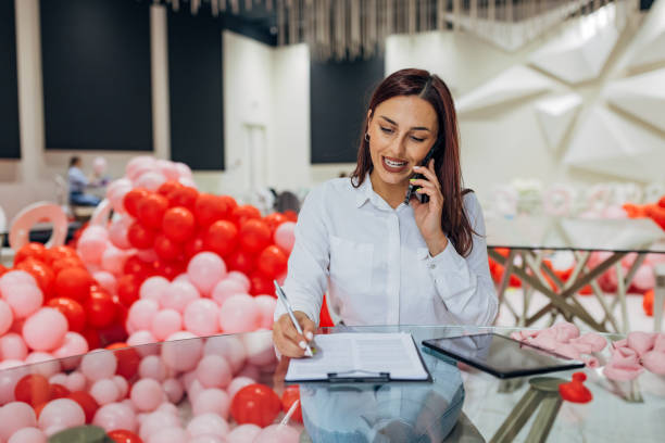 istock The decorator sits at the table in the restaurant and talks on the phone with the client, writes down a detailed plan for the decoration and organization of the party 2156169669