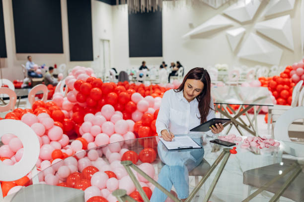 istock Female decorator sits at a table in a restaurant and uses a digital tablet that displays detailed plans for the decoration and organization of the party, which she writes down 2156169670