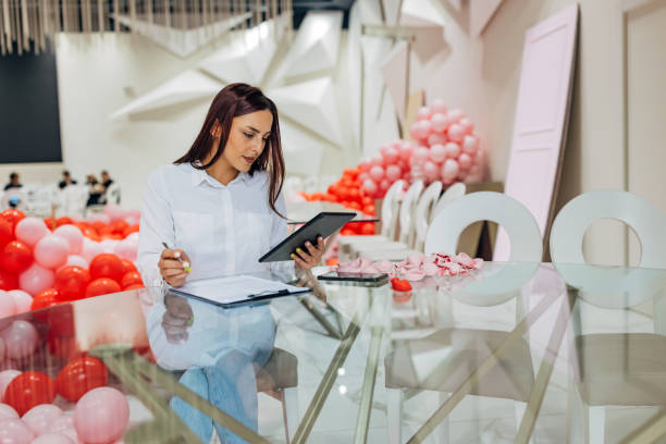 istock A decorator is sitting at a table in a restaurant using a digital tablet. The tablet shows detailed plans and sketches for the decoration and organization of the party 2156169701