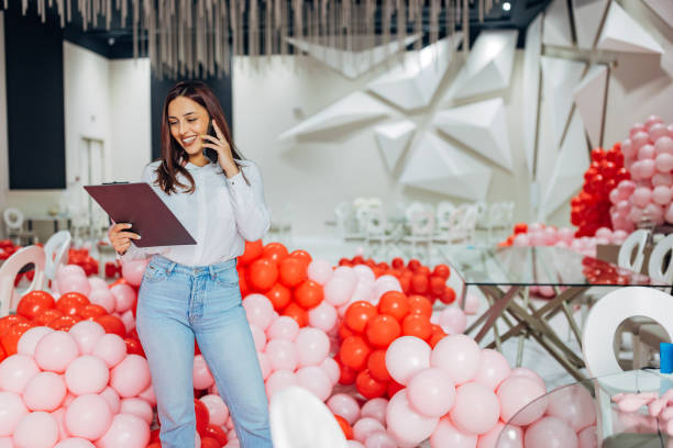 istock Carefree female event organizer talks on her mobile phone with new clients while she supervises the decoration of the party hall 2156170309
