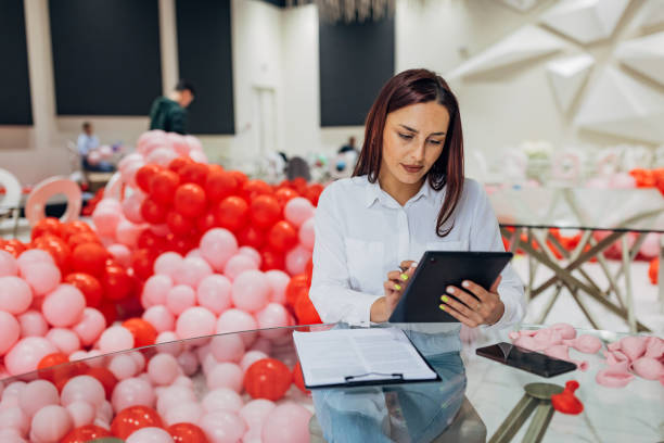 istock Female decorator is sitting at a table in a restaurant using a digital tablet. On the digital tablet are detailed plans and sketches for the decoration of the party 2156170355