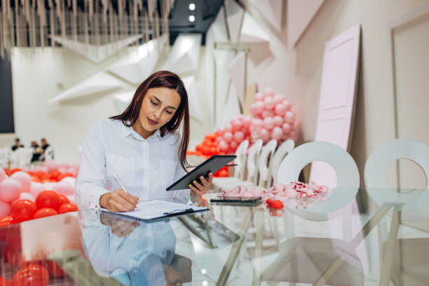 istock Female decorator is sitting at a table in a restaurant using a digital tablet. On the digital tablet are detailed plans and sketches for the organization of the party 2156170358