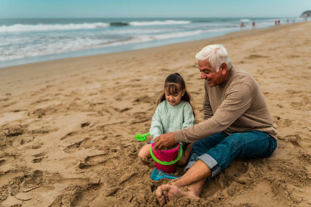 Grandfather playing with granddaughter on sand at beach