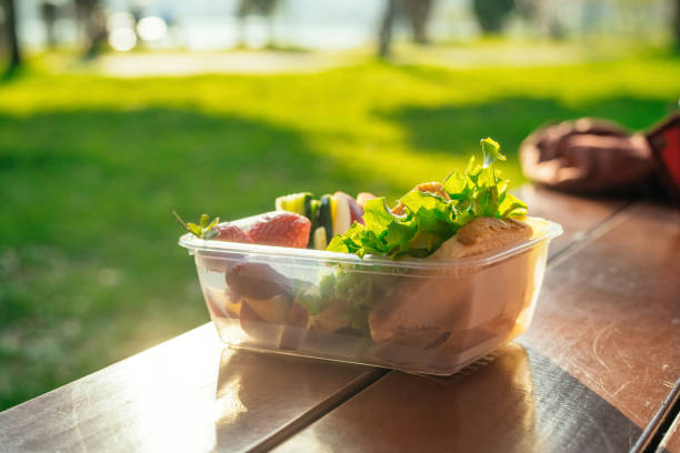 istock Plastic container with sandwich, vegetables and fruits on a table in a park in sunset 2156175304