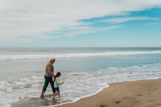 istock Grandfather talking and walking with granddaughter at beach 2156176789