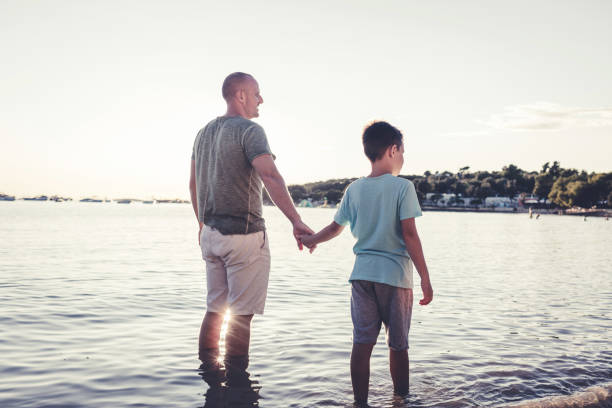 Father holding hands with son on summer beach vacation.