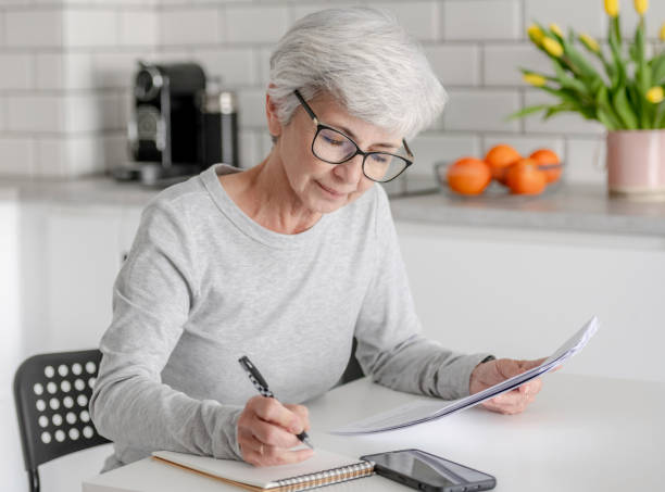 istock Elderly Woman Reviews Documents And Makes Notes 2156179527