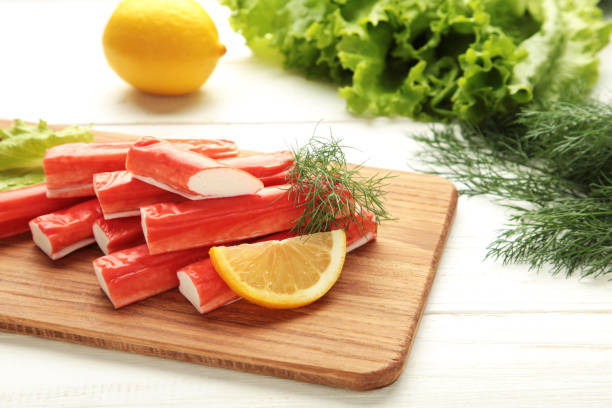 Fresh crab sticks with lemon on cutting board on white background.